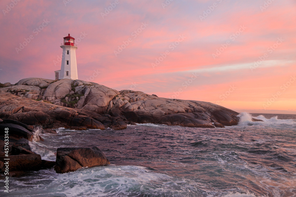 Peggy’s Cove Lighthouse illuminated at sunset with dramatic waves on the foreground, Nova Scotia, Canada
