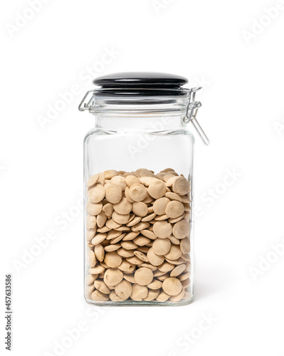 Dog treats in glass jar with snap lid. Airtight translucent storage container filled with many pet treat pellets in circular disc shapes and pale yellow color. Selective focus.  Isolated on white.