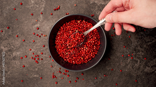 TOP VIEW: Human hand takes pink pepper seeds by a spoon from a dish