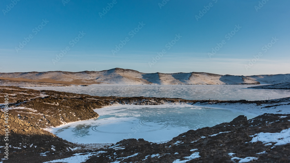 A frozen lake in the form of an ice heart. Snow lies on the ground, devoid of vegetation. Nearby is Lake Baikal. A mountain range against the blue sky. Siberia A frozen lake in the form of an ice heart. Snow lies on the ground, devoid of vegetation. Nearby is Lake Baikal. A mountain range against the blue sky. Siberia