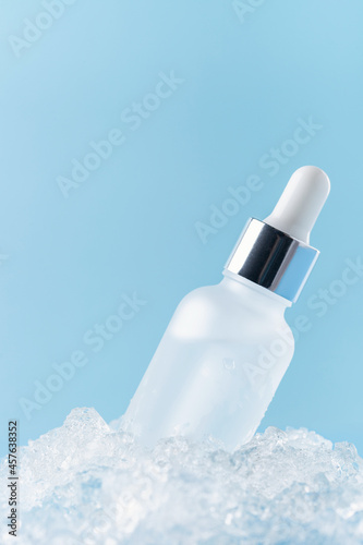 Serum bottle on ice blue background. Natural cosmetics concept