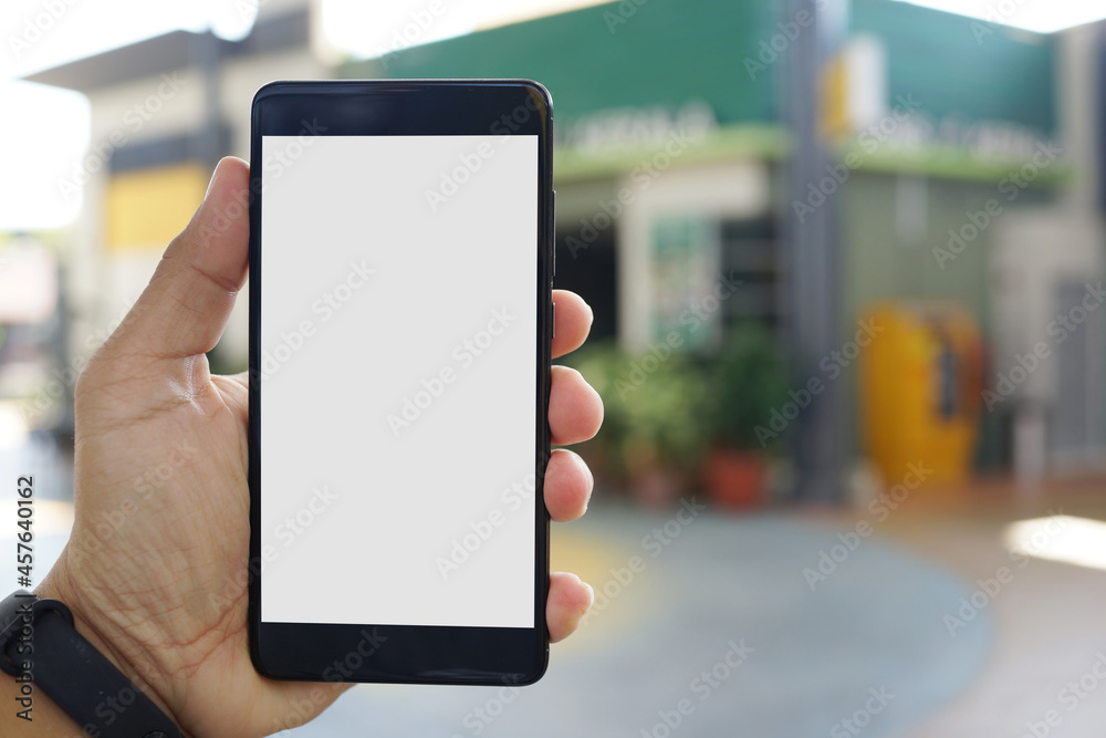 Adult hand holding a smartphone outside a store with blank copy space screen for text message or information content Adult hand holding a smartphone outside a store with blank copy space screen for text message or information content