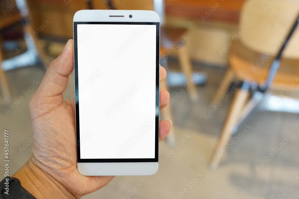 Adult hand holding a smartphone in a cafe restaurant with blank copy space screen for text message or information content Adult hand holding a smartphone in a cafe restaurant with blank copy space screen for text message or information content