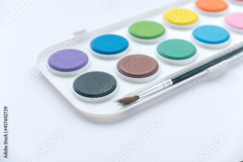 Selective focus of colorful watercolor palette with brush on white background.
