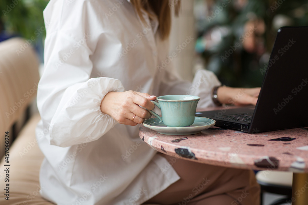 cup of coffee and laptop close-up on table in cafe. hand of business woman with nude manicure takes mug. freelance work cup of coffee and laptop close-up on table in cafe. hand of business woman with nude manicure takes mug. freelance work