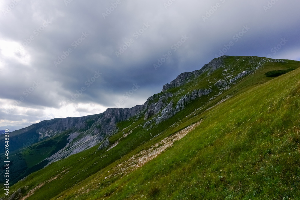 steep green rocky mountain with gray rain clouds