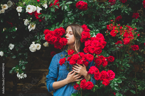 young woman near the bush of red roses in a garden