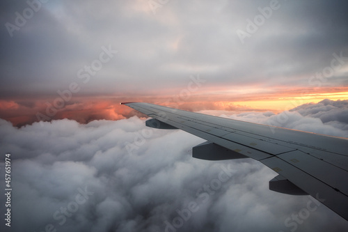 View from the airplane window to thick clouds and a beautiful sunset. Evening flight. The wing of the plane is high above the ground. Rest abroad.