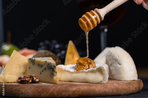 Sweet viscous honey is poured onto Camembert with walnuts. Various types of cheese and fruits lie side by side on the table. Close-up.