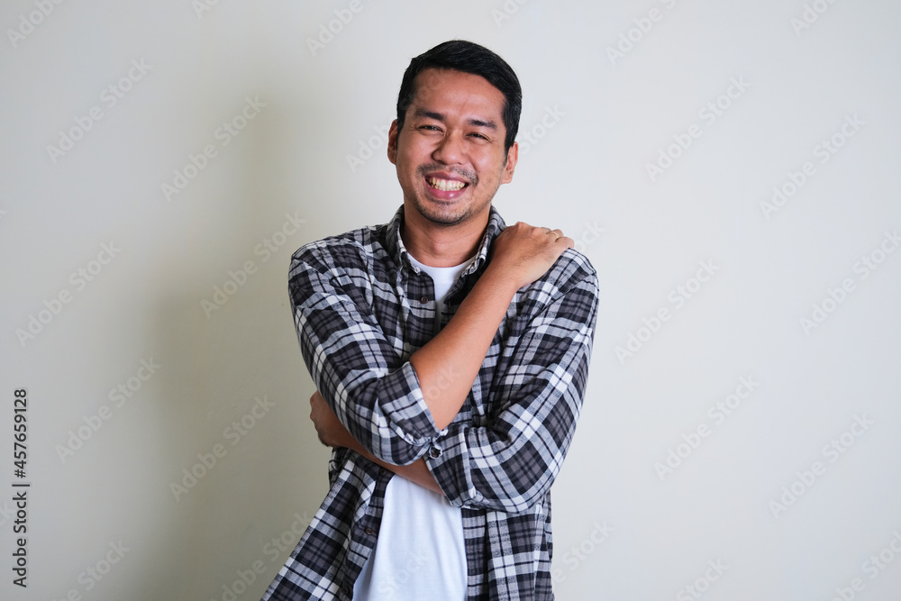 Adult Asian man hugging his self with happy face expression