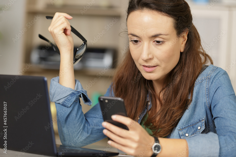 woman with phone and laptop at table