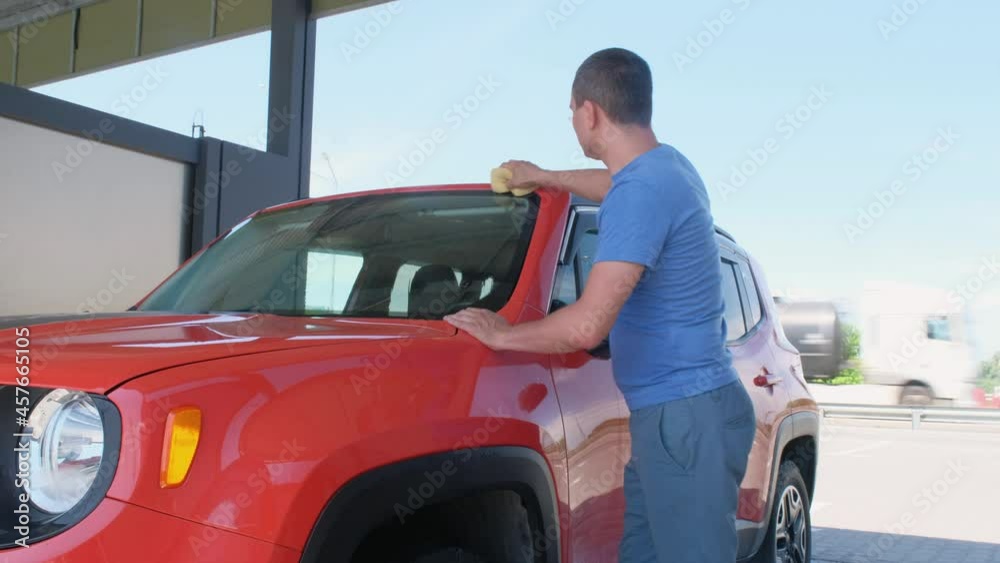 A man washes his car with a sponge at a car wash. Car in foam, washing the car with soap A man washes his car with a sponge at a car wash. Car in foam, washing the car with soap