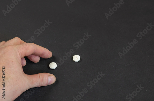Man's hand takes two white pills from a black surface. Health care and traditional medicine. An angled view from above. Selective focus.