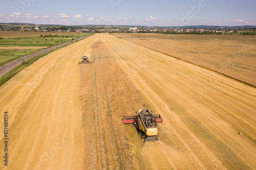 Aerial view of combine harvesters harvesting large yellow ripe wheat field.