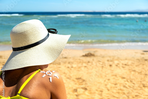 Back view of young woman tanning at the beach with sunscreen cream in sun shape on her shoulder. UV sunburn protection and sunblock skincare concept