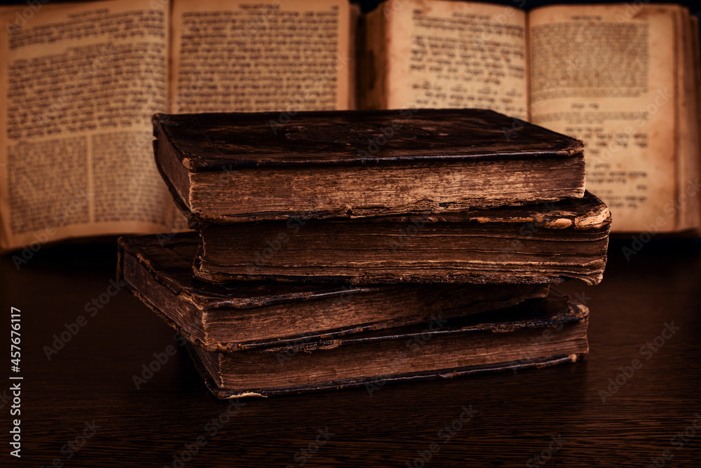 Stack of old worn shabby jewish books in leather binding and open blurred Torah in the background in the dark. Closeup. Selective focus.