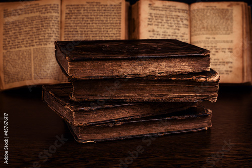 Obraz na płótnie Stack of old worn shabby jewish books in leather binding and open blurred Torah in the background in the dark. Closeup. Selective focus. w salonie
