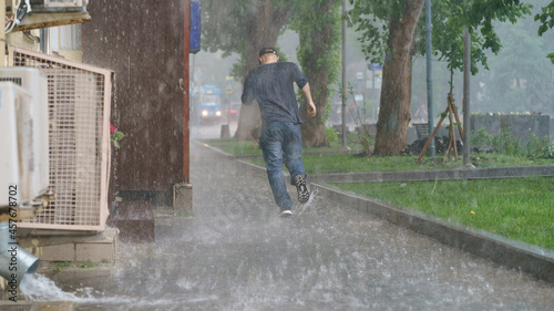 Raining day in the city at summer time. A wet young man running in the rain. Texture of strong, fresh and powerful water drops and sprays. Puddle with ripple on Moscow road. Power, energy in nature