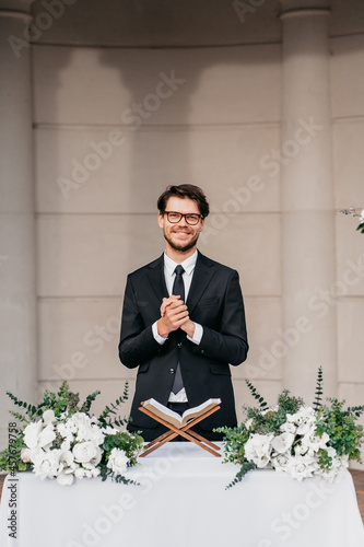 Portrait of young cheerful Caucasian marriage officiant during wedding ceremony