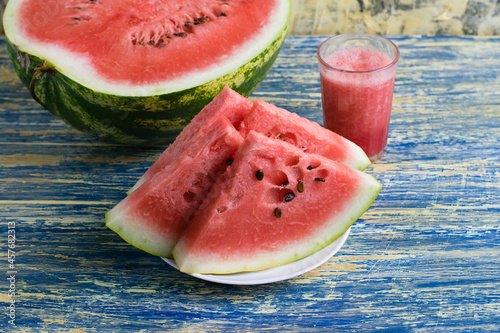 Half sweet watermelon, smoothie in a glass and sliced watermelon on a white plate on a blue background