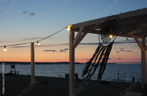 Breeze place for rest: twilight waterfront terrace, on the shoreline, chill area zone on the beach Baltic Sea: cozy wood summer house, decorated with a luminous garland and the feather dream catcher