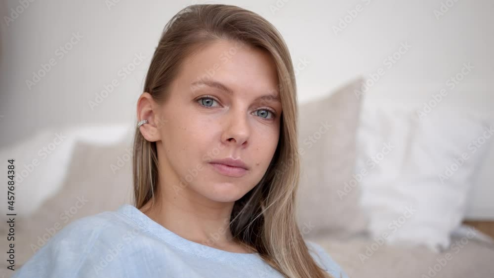 Serious blonde woman with grey eyes sitting on background of bed and pillows. Closeup of beautiful woman with long hair at her sleeping room. Gimbal shot Serious blonde woman with grey eyes sitting on background of bed and pillows. Closeup of beautiful woman with long hair at her sleeping room. Gimbal shot