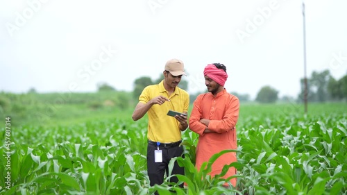 Young indian banker or agronomist showing some detail to farmers in smartphone at agriculture field.