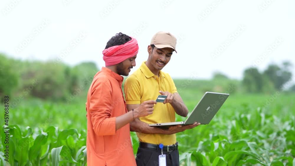 Young indian banker or agronomist showing some detail to farmers in laptop at agriculture field.