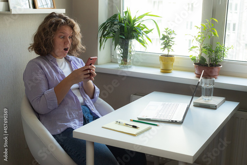 woman working at home with laptop and white table notebook pen and phone suprising photo