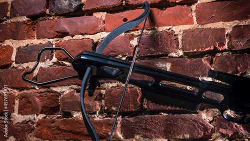 A modern compound crossbow handgun on the red brick wall background. Old weapon concept.