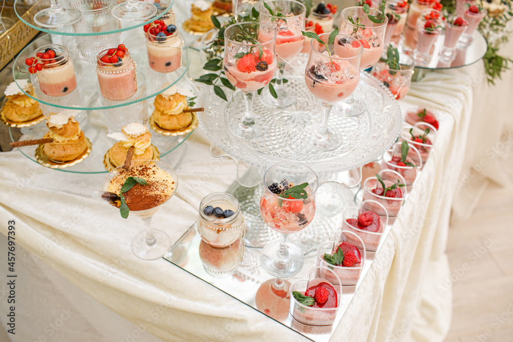 Wedding. Candy bar. White wedding cake decorated by flowers standing of festive table with deserts, strawberry tartlet and cupcakes.