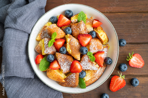 Kaiserschmarrn - traditional austrian pancake dessert with fresh berries and powdered sugar on a dark wooden background. Sweet breakfast. Copy space.