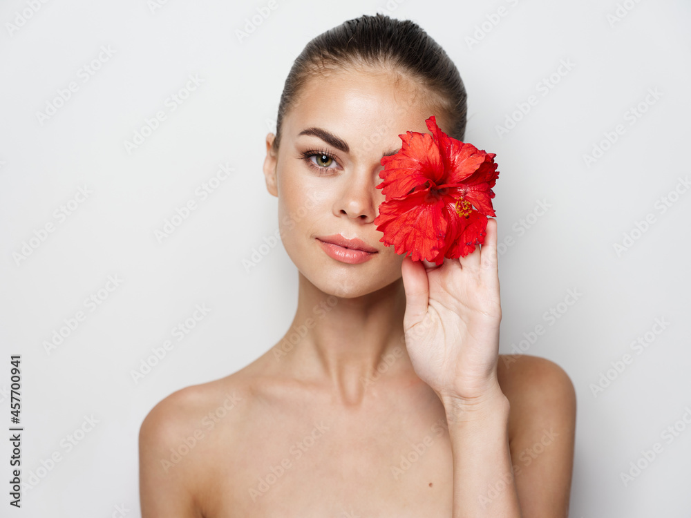 attractive woman with bare shoulders holding a red flower in her hand in front of her face attractive woman with bare shoulders holding a red flower in her hand in front of her face