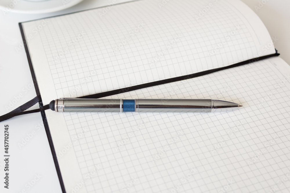 The concept of a workplace with an open notebook and a metal pen on a modern white table. Minimalism. Side view from above. The concept of a workplace with an open notebook and a metal pen on a modern white table. Minimalism. Side view from above.