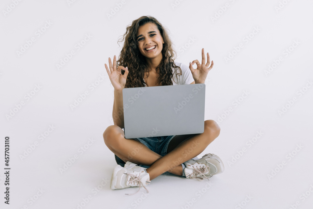 Cheerful young woman holding laptop with blank screen and showing okay gesture over white background Cheerful young woman holding laptop with blank screen and showing okay gesture over white background