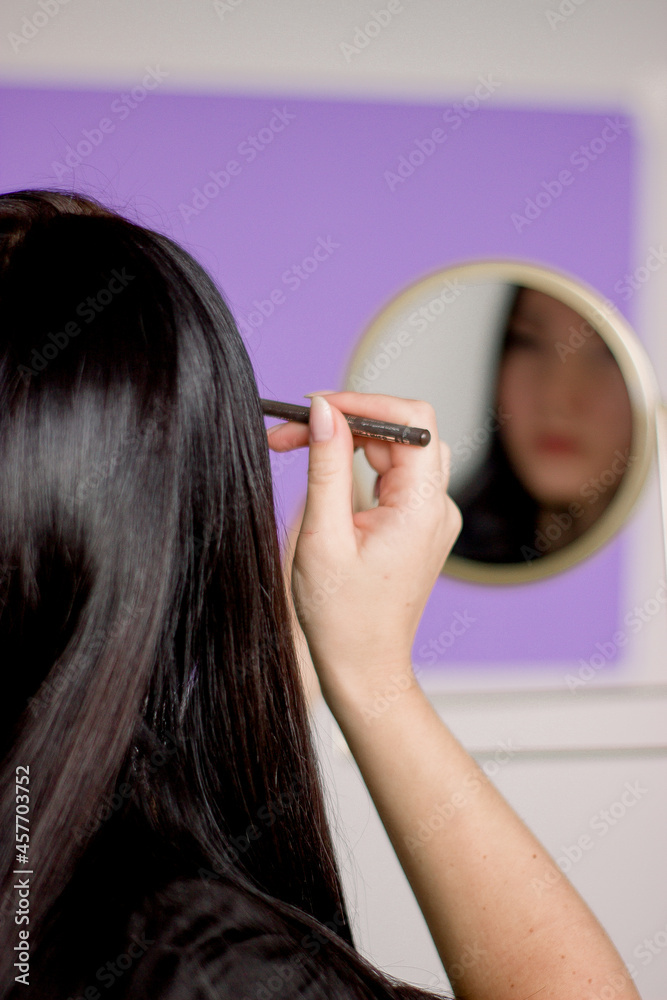 Fototapeta premium A girl does makeup while looking in the mirror