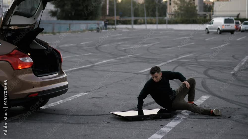 A man drops a new purchased TV on a supermarket parking and falls, unsuccessfully delivers it to the car trunk, funny fail A man drops a new purchased TV on a supermarket parking and falls, unsuccessfully delivers it to the car trunk, funny fail