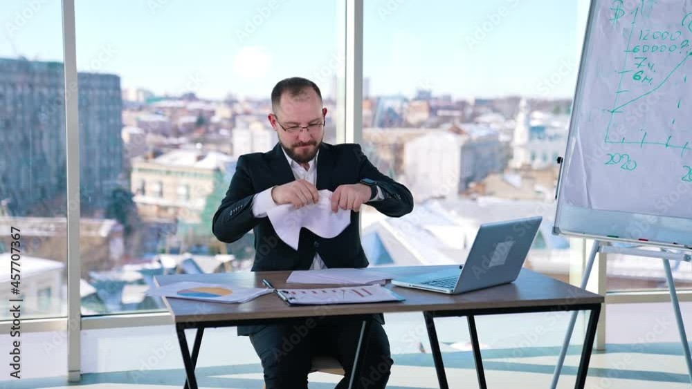 Nervous entrepreneur on his workplace. Businessman in costume sitting at the desk and throwing papers. Business problems. Nervous entrepreneur on his workplace. Businessman in costume sitting at the desk and throwing papers. Business problems.