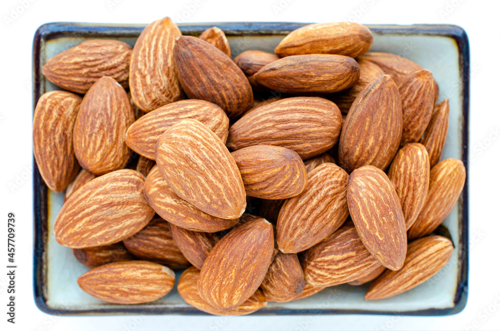 Fototapeta premium Closed up dry organic almond seed pile in ceramic bowl isolated on white background