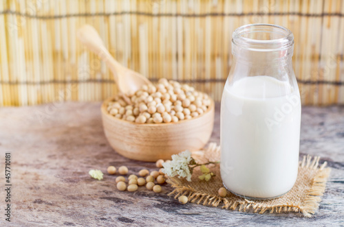 Closed up fresh organic homemade soybean milk in glass bottle over blur soybean seed pile in wooden bowl and spoon on grunge background in soft light tone