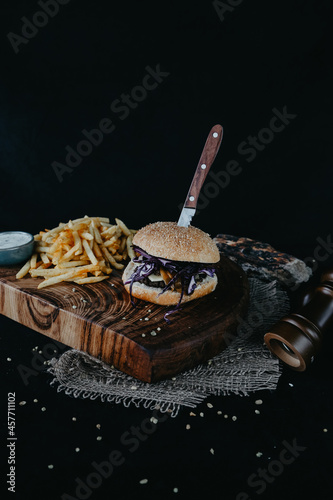 Hamburger on wooden plate with fries on black background