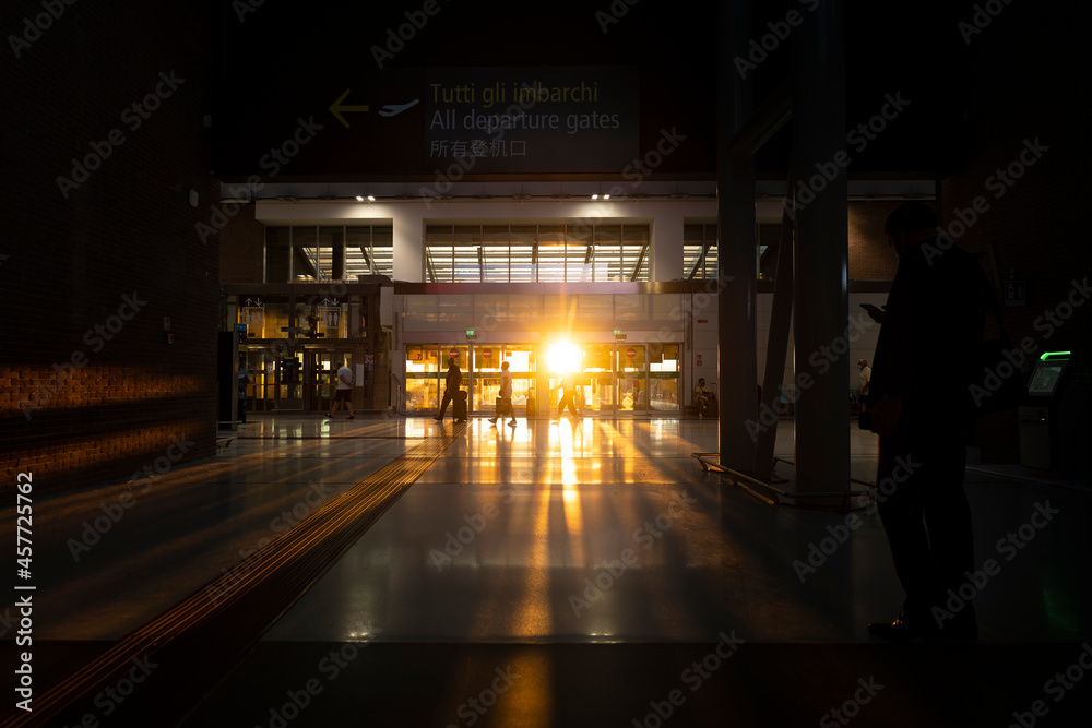 Silhouette of some tourists walking inside an airport terminal during a stunning sunset. Travel concept during the Covid-19 pandemic.