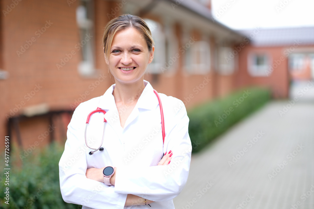 Portrait of young smiling female doctor with red stethoscope near clinic Portrait of young smiling female doctor with red stethoscope near clinic