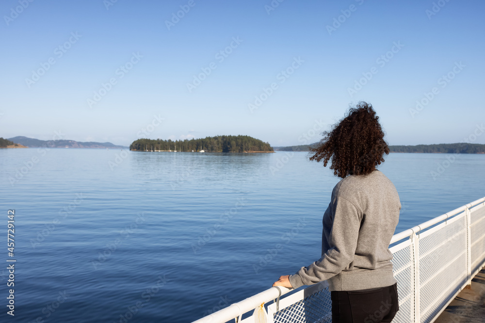 White Caucasian Adult Woman watching the Canadian Nature Scenery from a ferry boat. West Coast of Pacific Ocean. Vancouver Island, British Columbia, Canada. White Caucasian Adult Woman watching the Canadian Nature Scenery from a ferry boat. West Coast of Pacific Ocean. Vancouver Island, British Columbia, Canada.