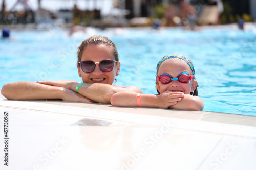Little girl in swimming goggles and mother lying on side of pool