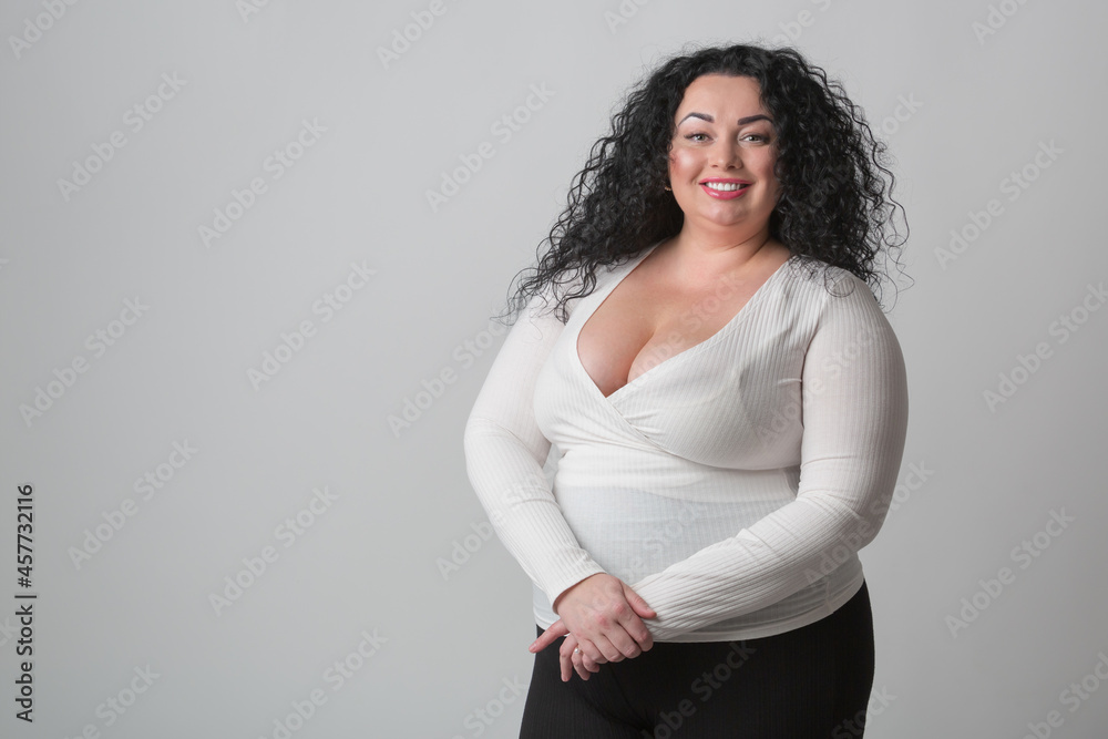 Plus size woman with deep cleavage and big breast posing in studio with  happy toothy smile. Overweight female model with curly dark hair looking in  camera Stock Photo