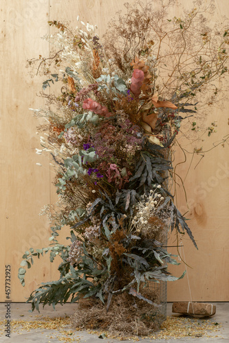 Large floral arrangement bouquet of dried flowers on the background of a wood wall and cement floor. The concept of inspiration, congratulations, autumn season, studio flower decoration.