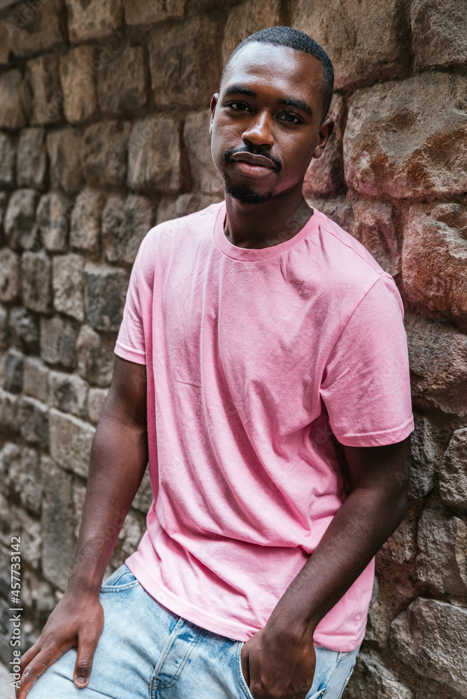 vertical portrait of an african young man. He is looking at camera with a stone wall on the background