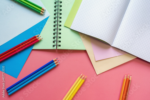  School and hobby concepts. Colored paper sheets, colored pencils and notebooks on pink paper background. Copy space