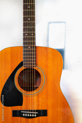 Yellow guitar standing upright position with partial view of a white door in the back 